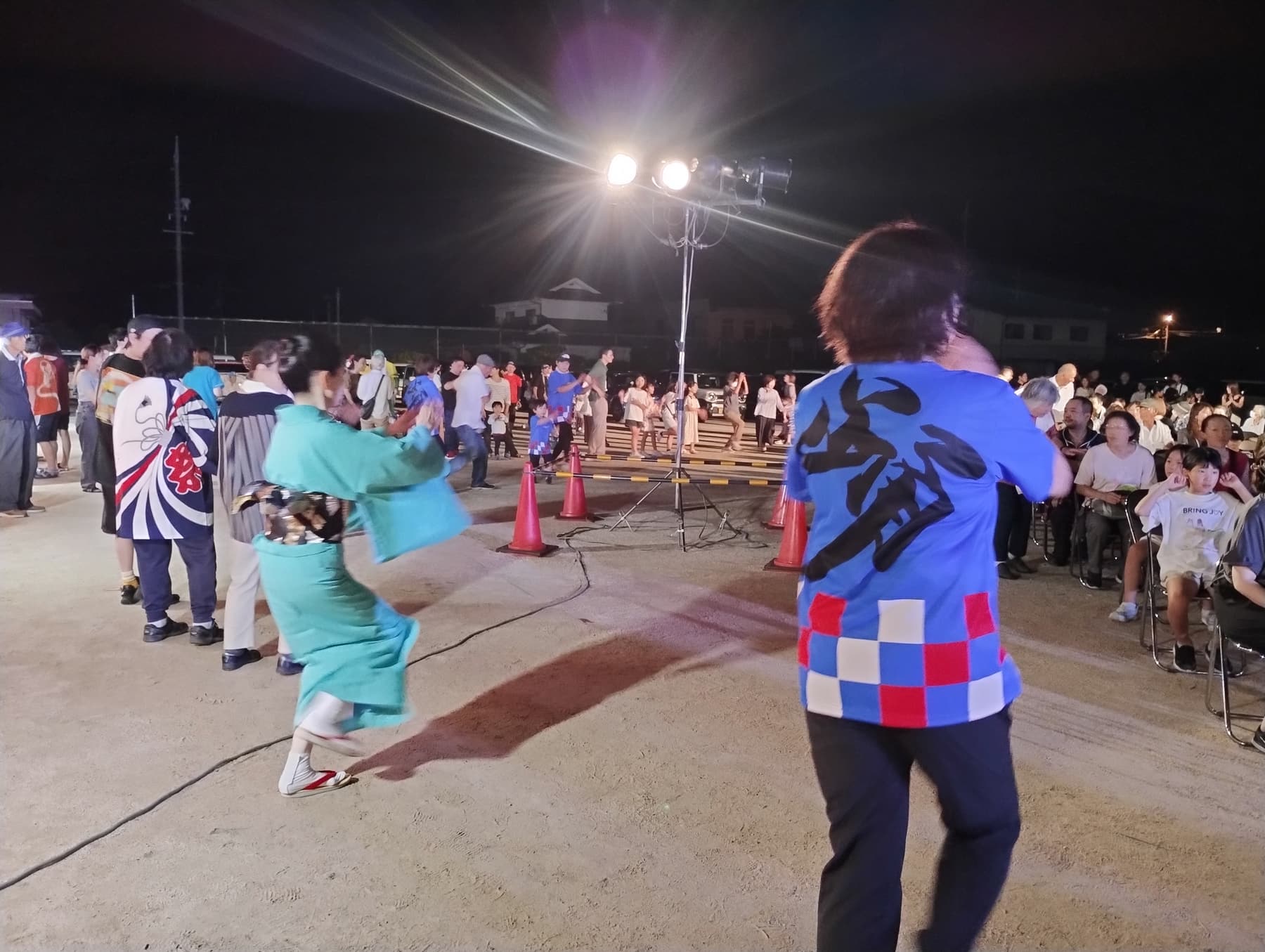 夜の北川小学校の運動場で、法被や浴衣の人たちが輪になって踊っている